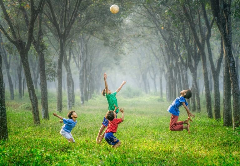 four children jumping in grass in a forest